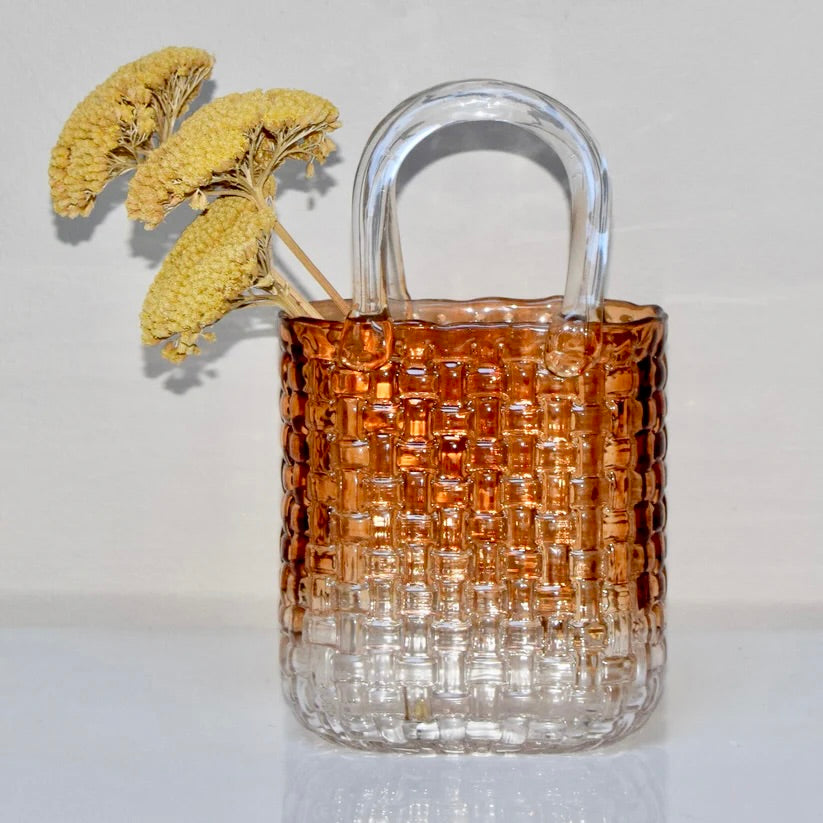 Amber glass vase with woven design and dried flowers on a white background.