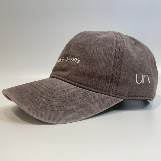 Brown washed cotton cap with 'made in the 90's' embroidery on the front and 'un' logo on the side.