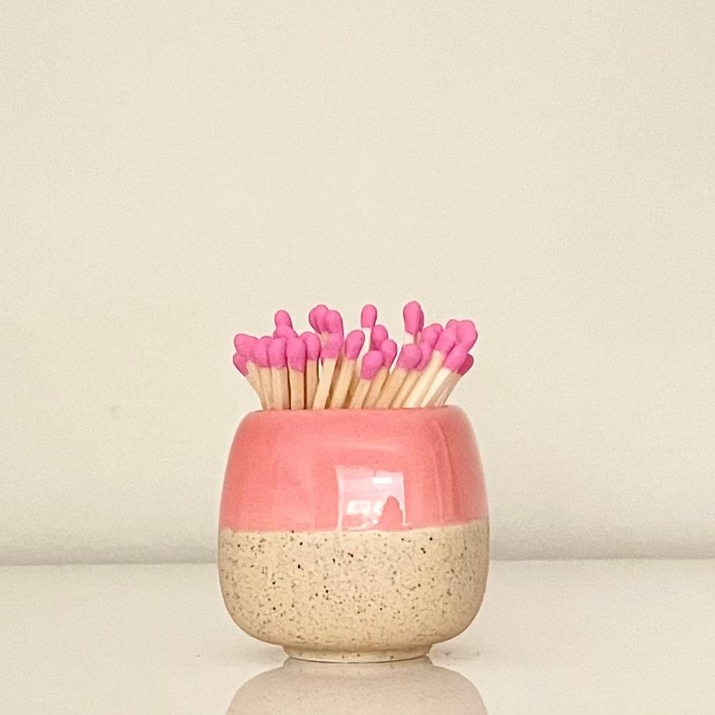 Pink ceramic match holder on a white surface.