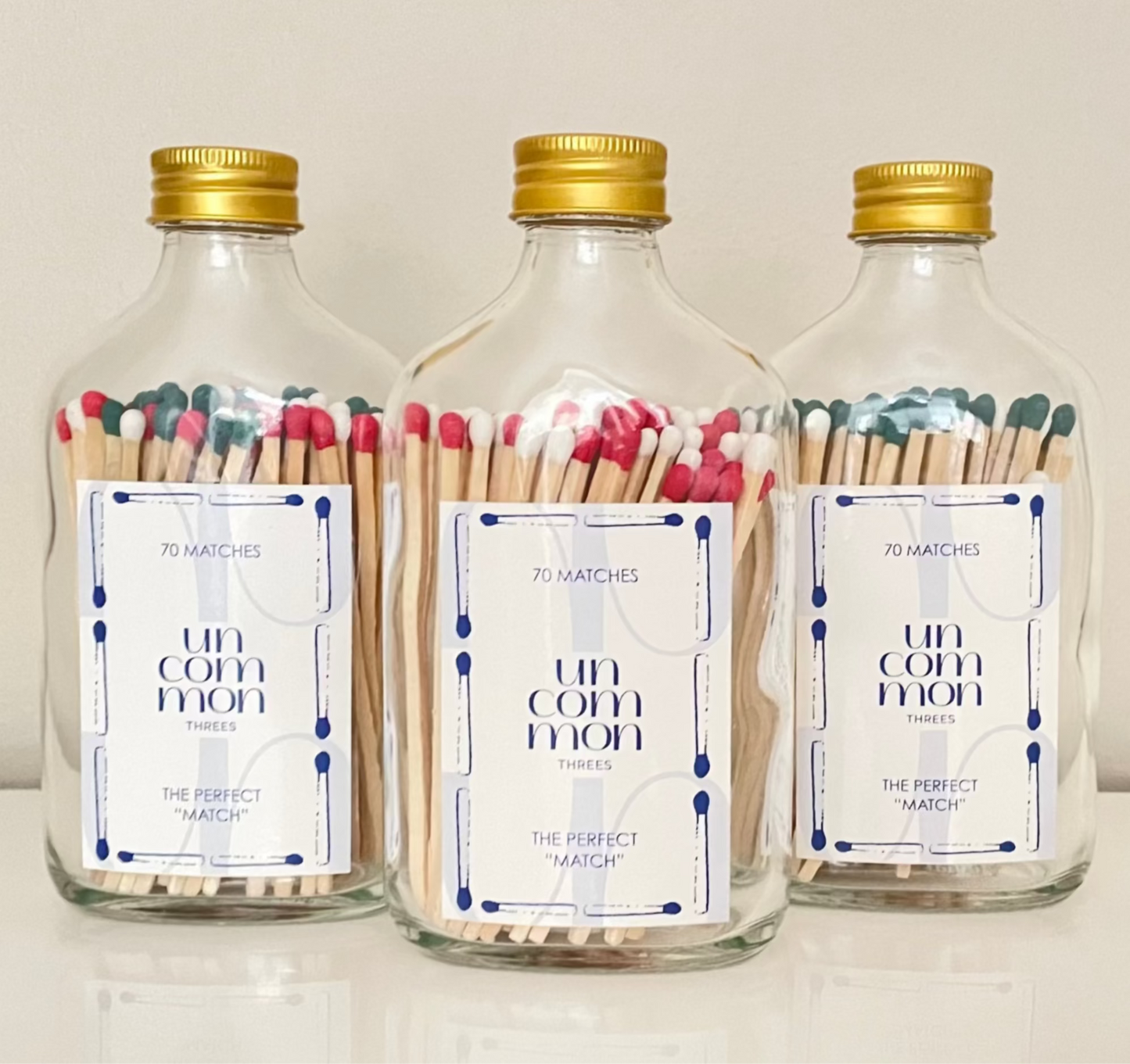 Gold lid glass bottles filled with 9.8 cm red, dark green and white matches on a white background.