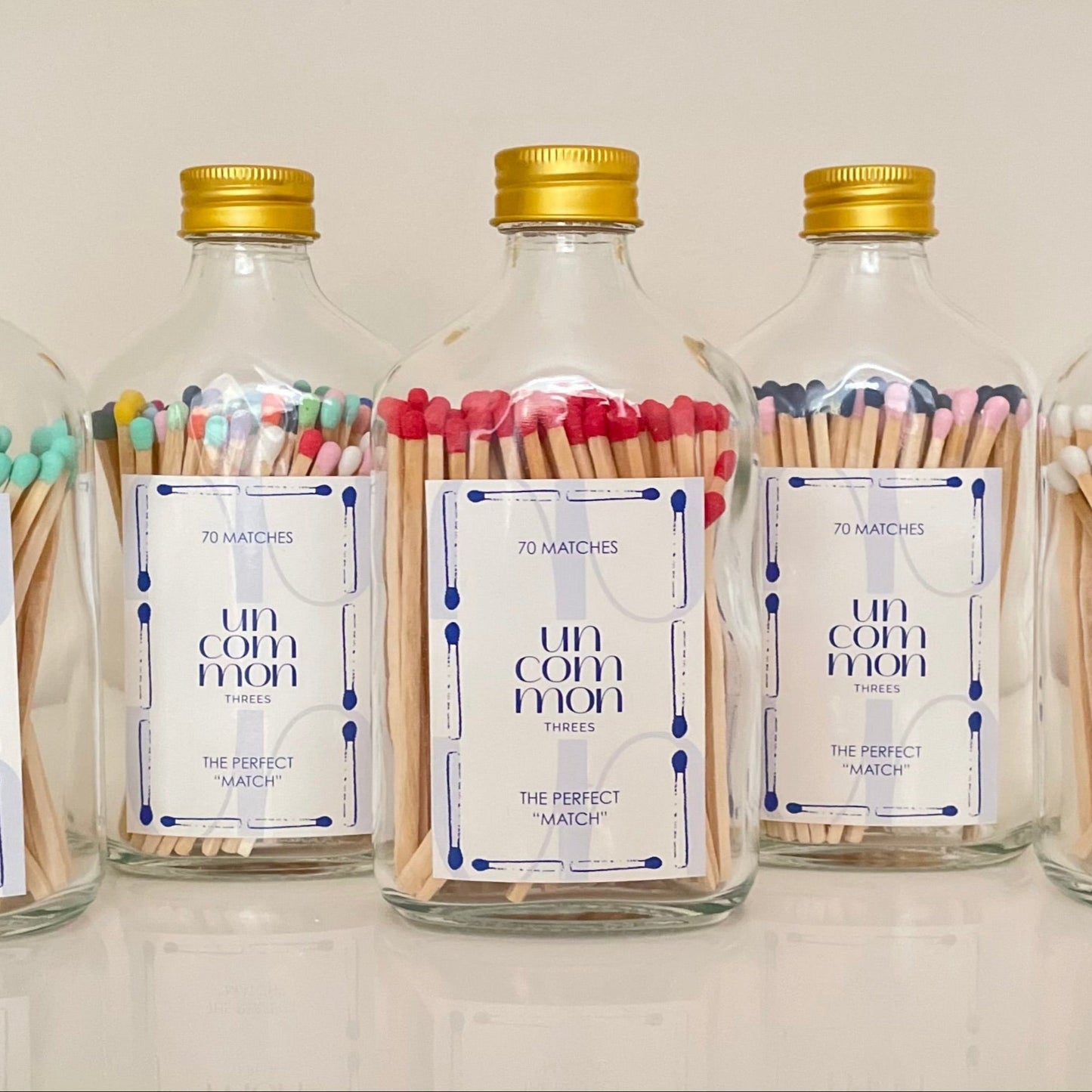 Five glass bottles with gold lids filled with colourful matches on a white background.