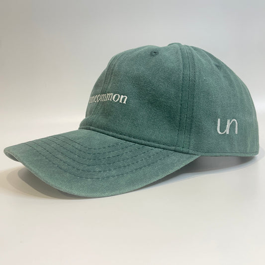 100% Green washed cotton cap with 'uncommon' white embroidery and 'un' side emblem.