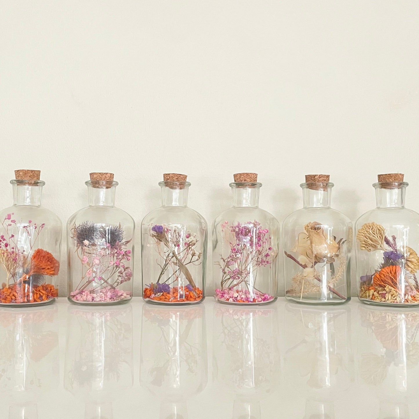 Glass bottles with cork lid filled with dried flowers on a light background.