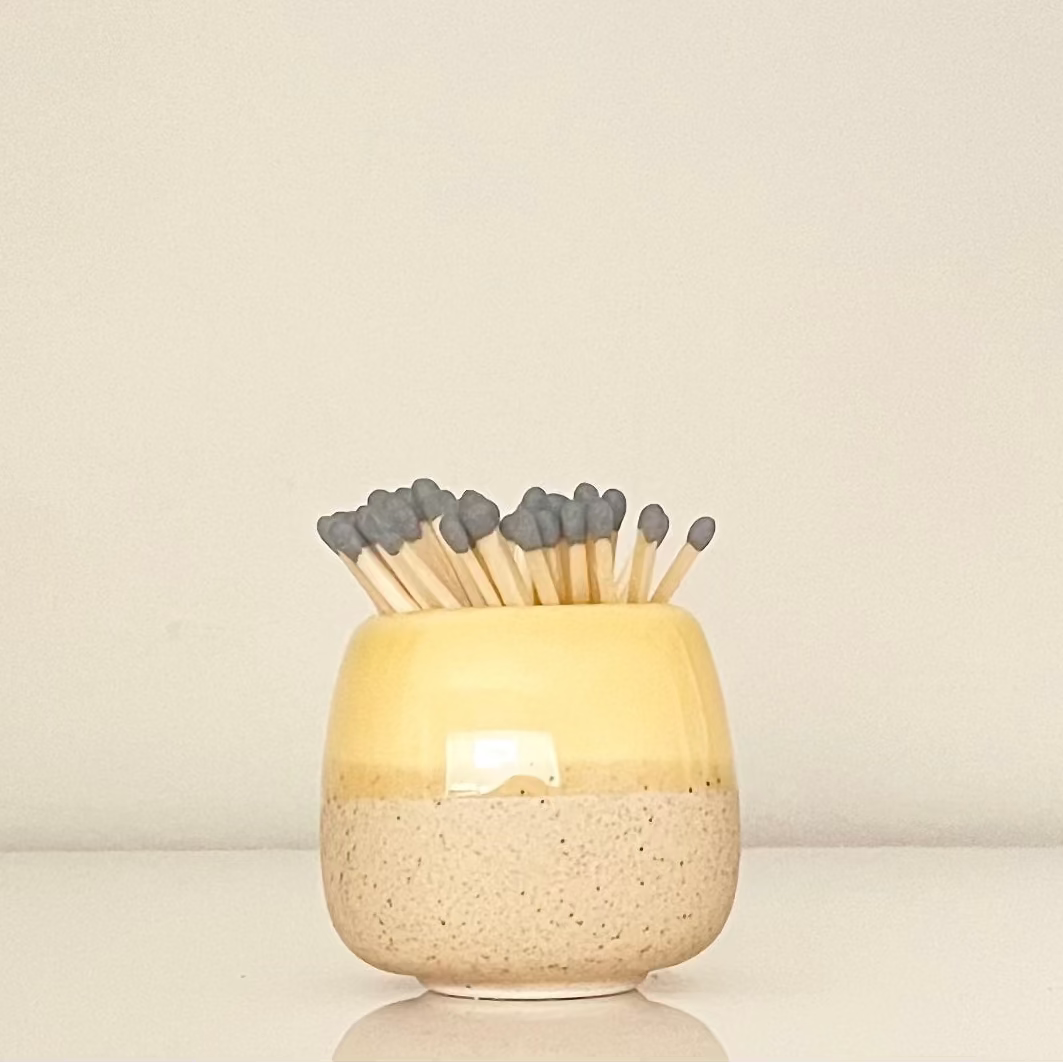 Yellow ceramic match holder on a white surface.