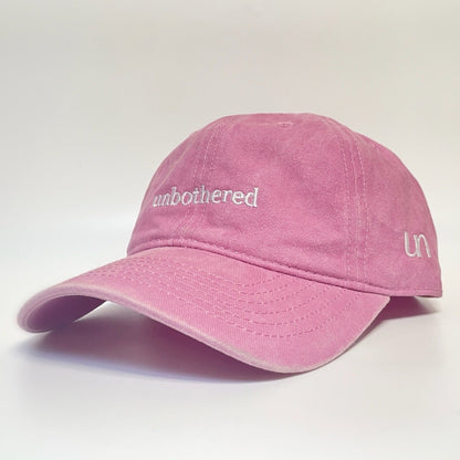 100% Pink washed cotton cap with 'unbothered' white embroidery with side emblem 'un'. 
