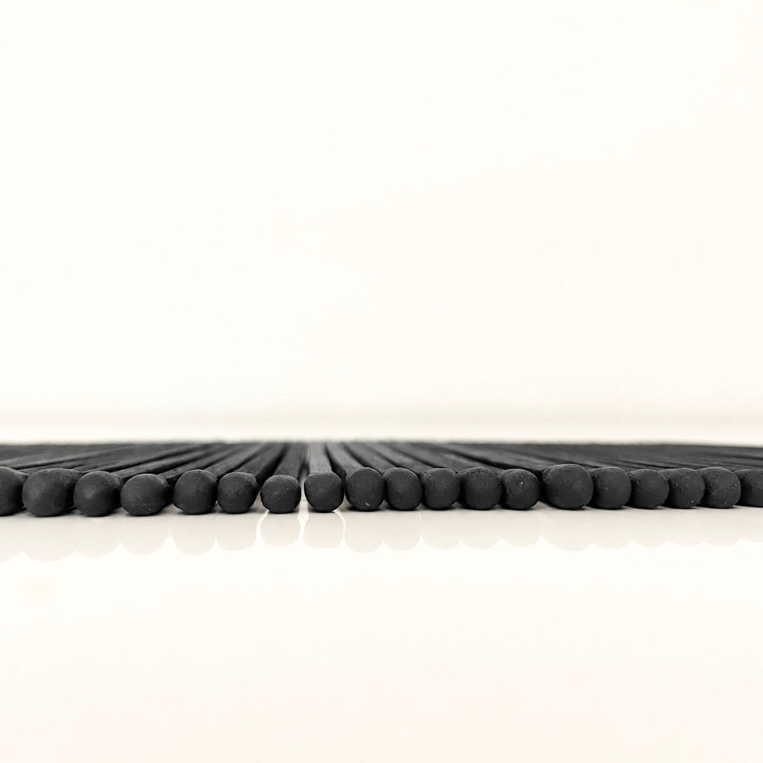 Line of 7.5 cm all black safety matches on a white surface.