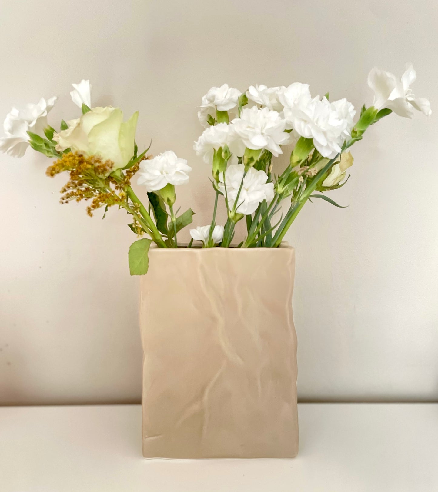 Ceramic beige vase with fresh flowers on a white surface. 