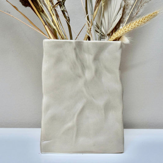 Beige ceramic vase with dried flowers n a white surface. 