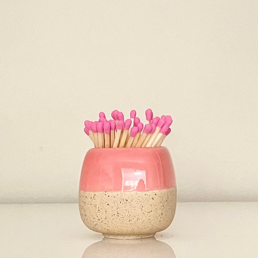 Pink ceramic match holder on a white surface.