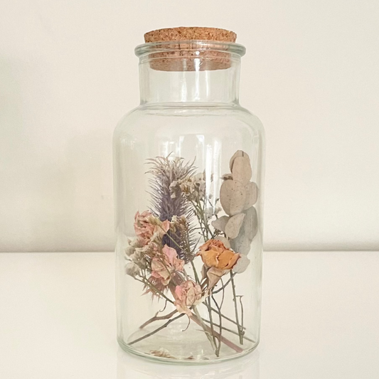 Glass bottle filled with yellow, pink and green dried flowers on a white background. 