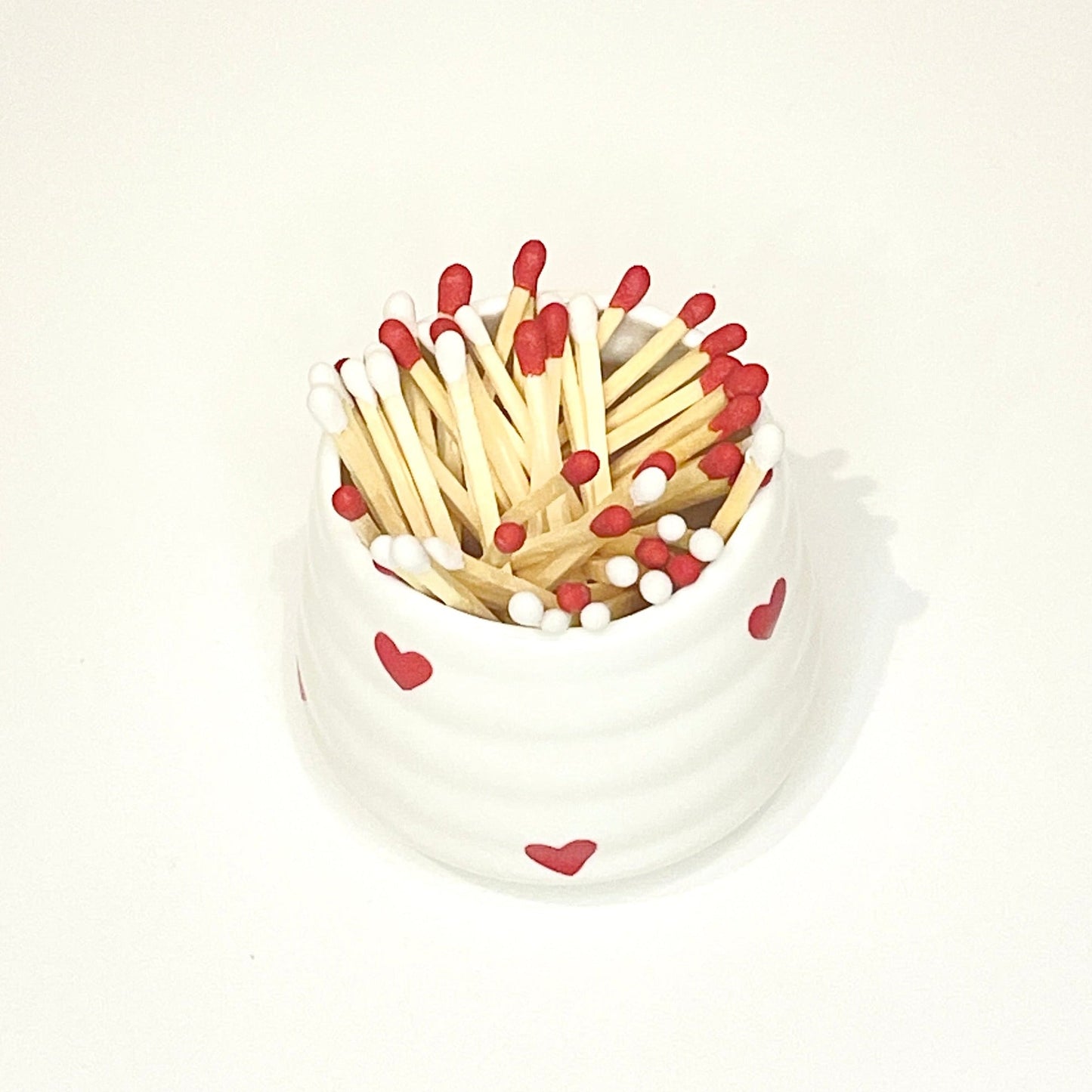 White ceramic holder/cup with heart designs filled with red and white matches on a white background.