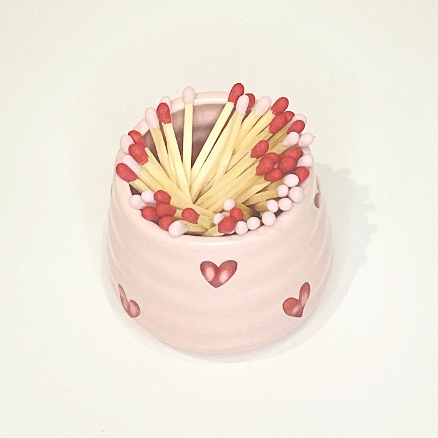 Pink ceramic holder/cup with heart designs filled with red and light pink matches on a white background.
