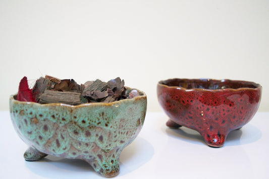 Two ceramic bowls, one green and the other red with speckled pattern, on a white background.