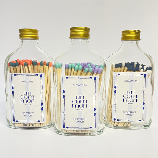 Three glass bottles with gold lids filled with two shades of colourful long safety matches on a white background.