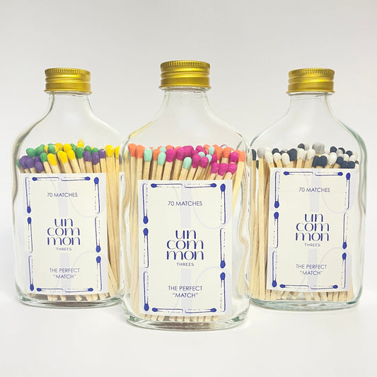 Three glass bottles with gold lids filled with colourful long safety matches on a white background.