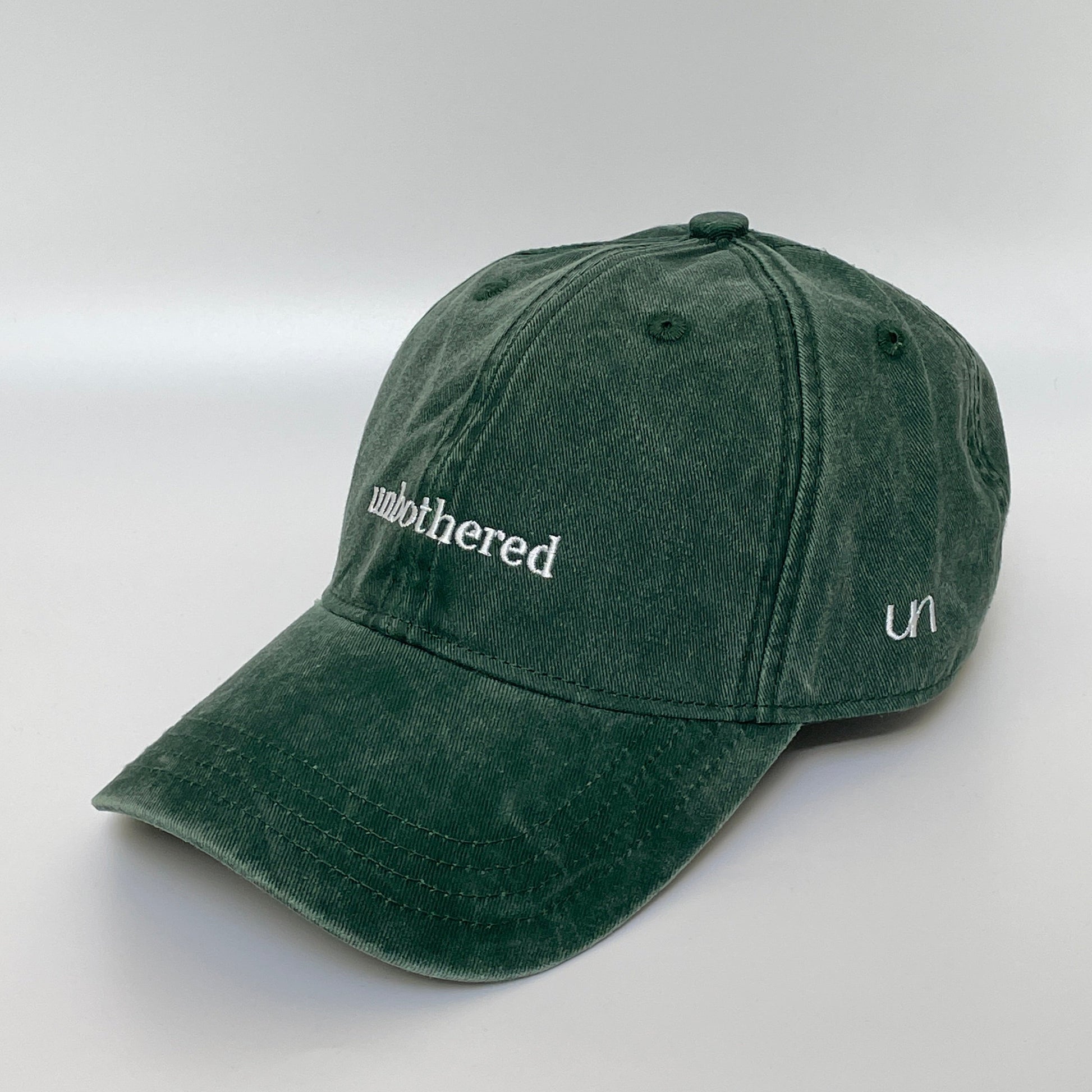 100% Green washed cotton cap with 'unbothered' white embroidery with side emblem 'un'. 