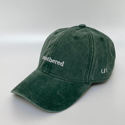 100% Green washed cotton cap with 'unbothered' white embroidery with side emblem 'un'. 