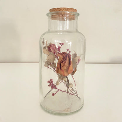 Giftable dreamy glass bottle with cork lid containing long lasting dried flowers on a light background.