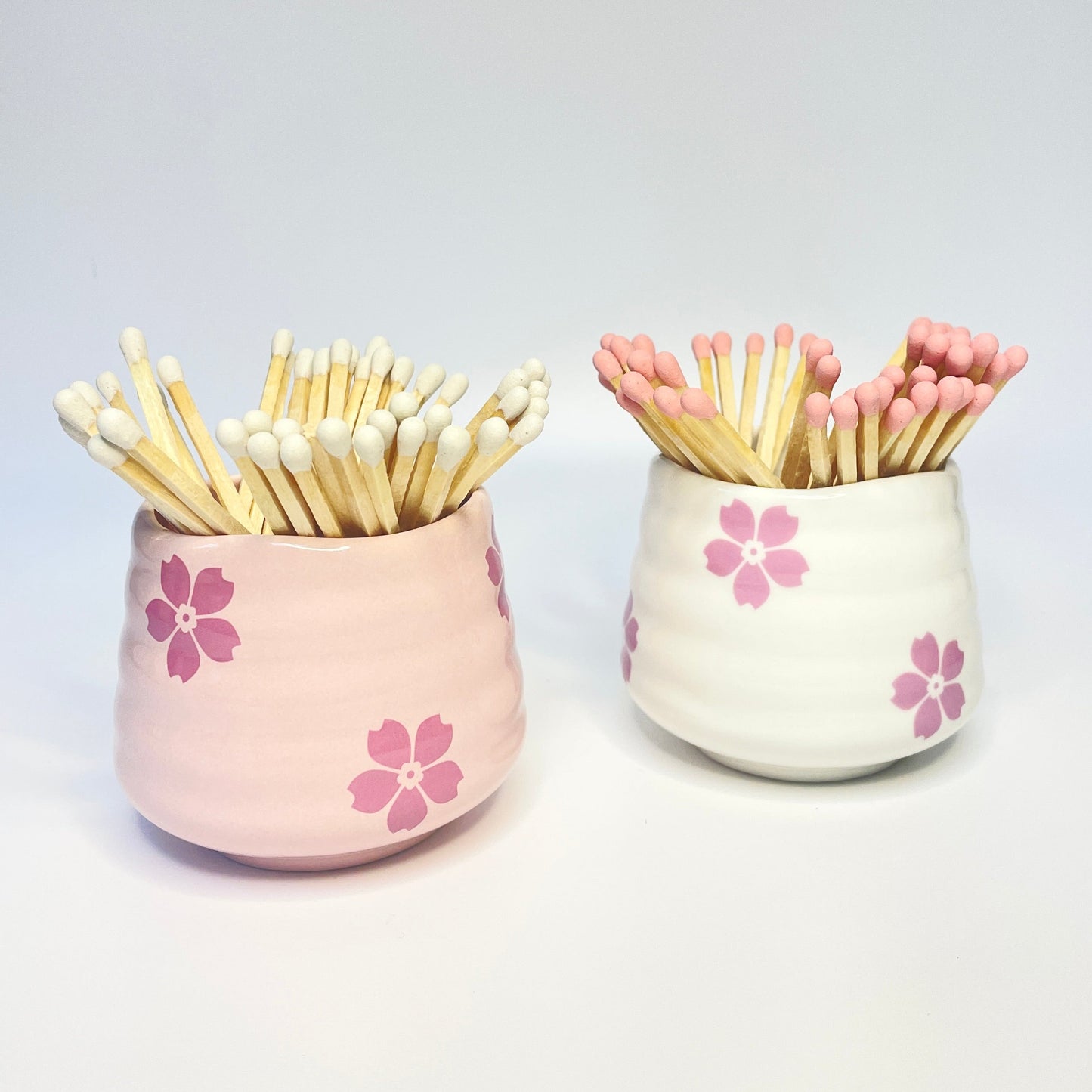 Pink and white ceramic flower safety match hodlers that can also be used as a coffee cup.