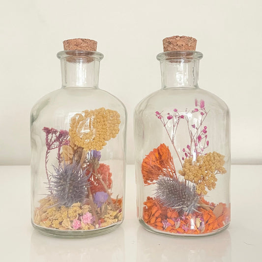Glass bottles filled with yellow, orange and purple dried flowers on a white background. 