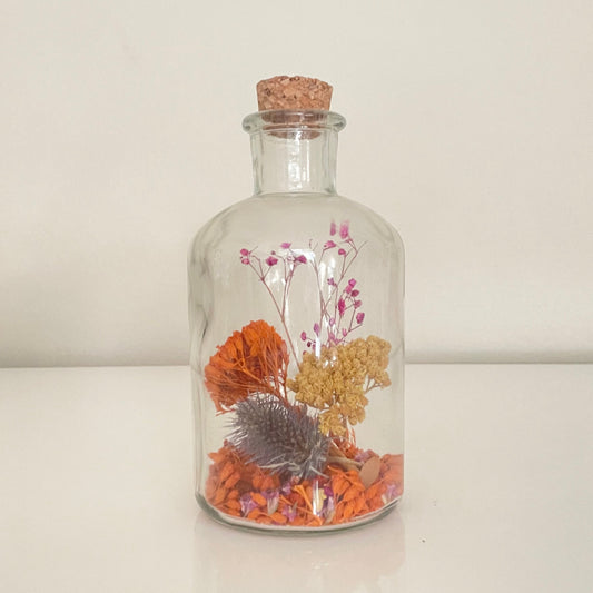 Glass bottle filled with yellow, orange and purple dried flowers on a white background. 