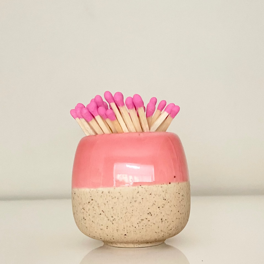 Pink ceramic match holder on a white surface.