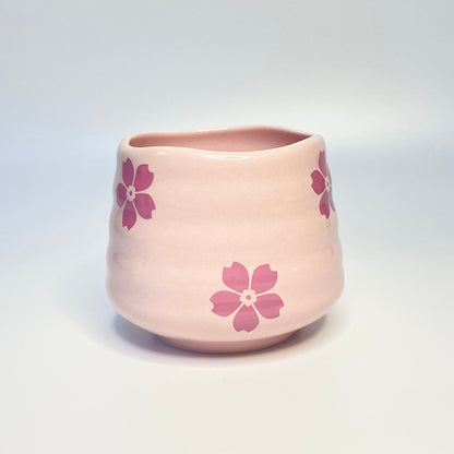 Pink ceramic coffee cup/match holder with floral patterns on a white surface.