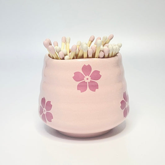 Pink ceramic holder/coffee cup with flower designs filled with light pink and white matches on a white background.