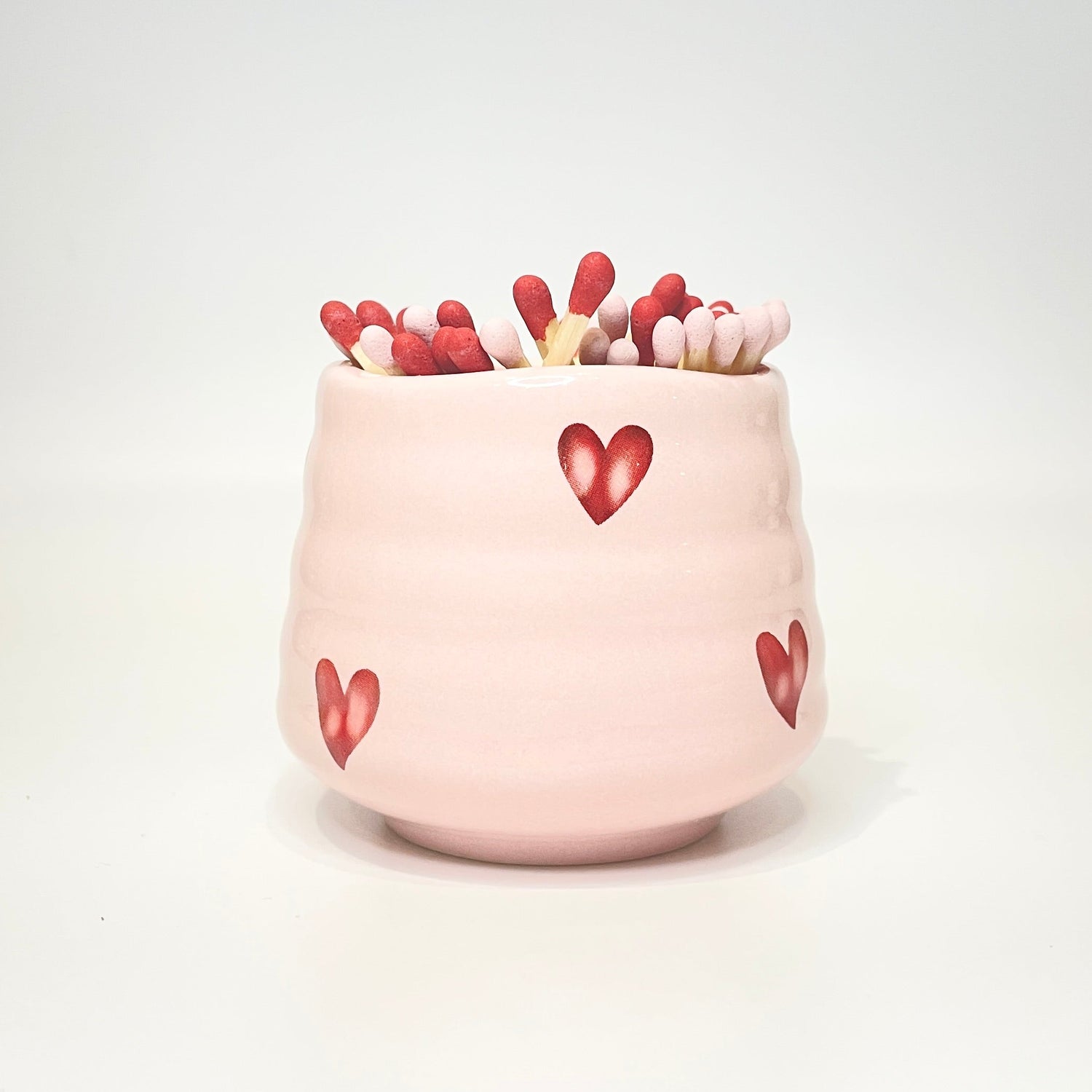 Pink ceramic holder/cup with heart designs filled with red and light pink matches on a white background.