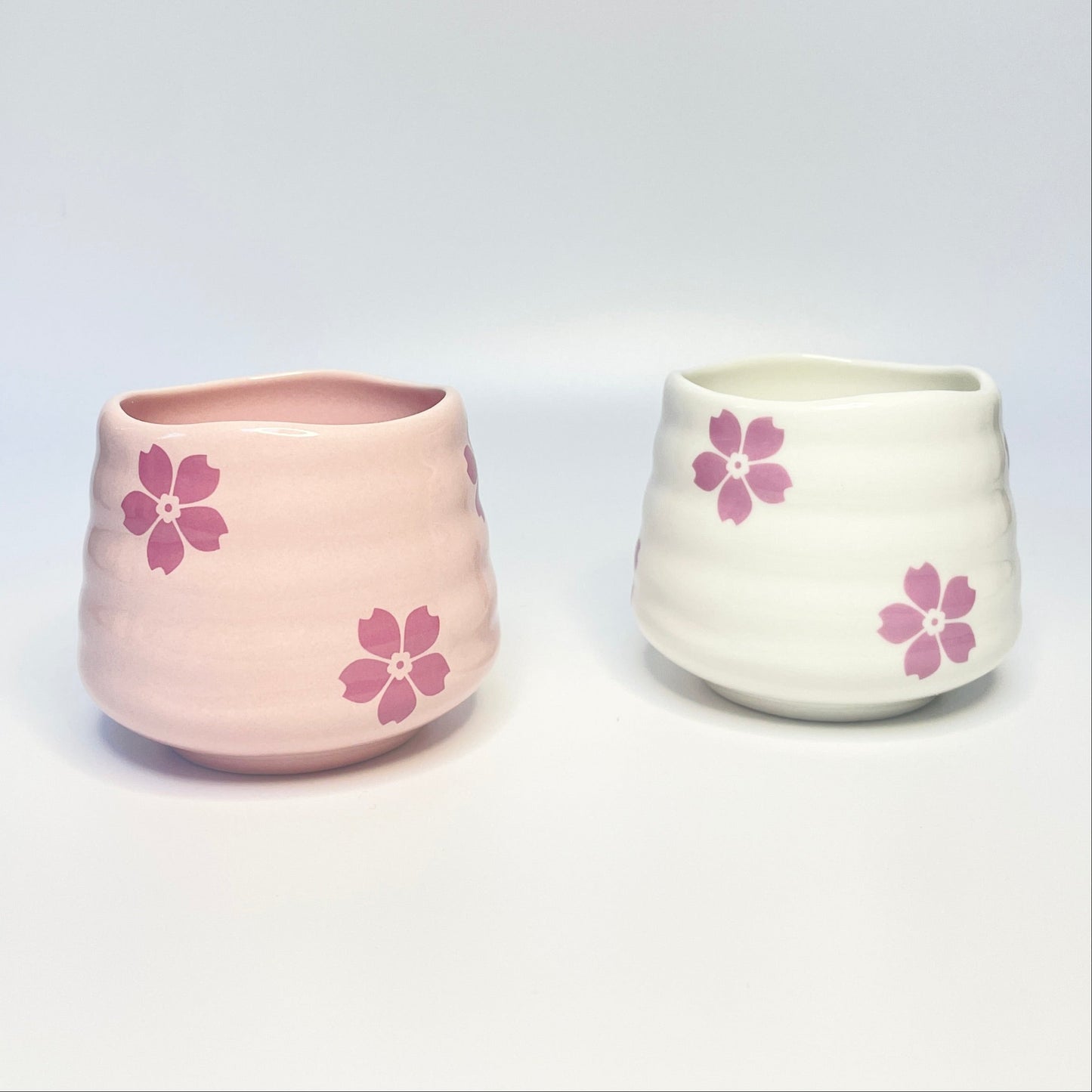 Two ceramic cups/match holders with pink floral designs on a white surface.