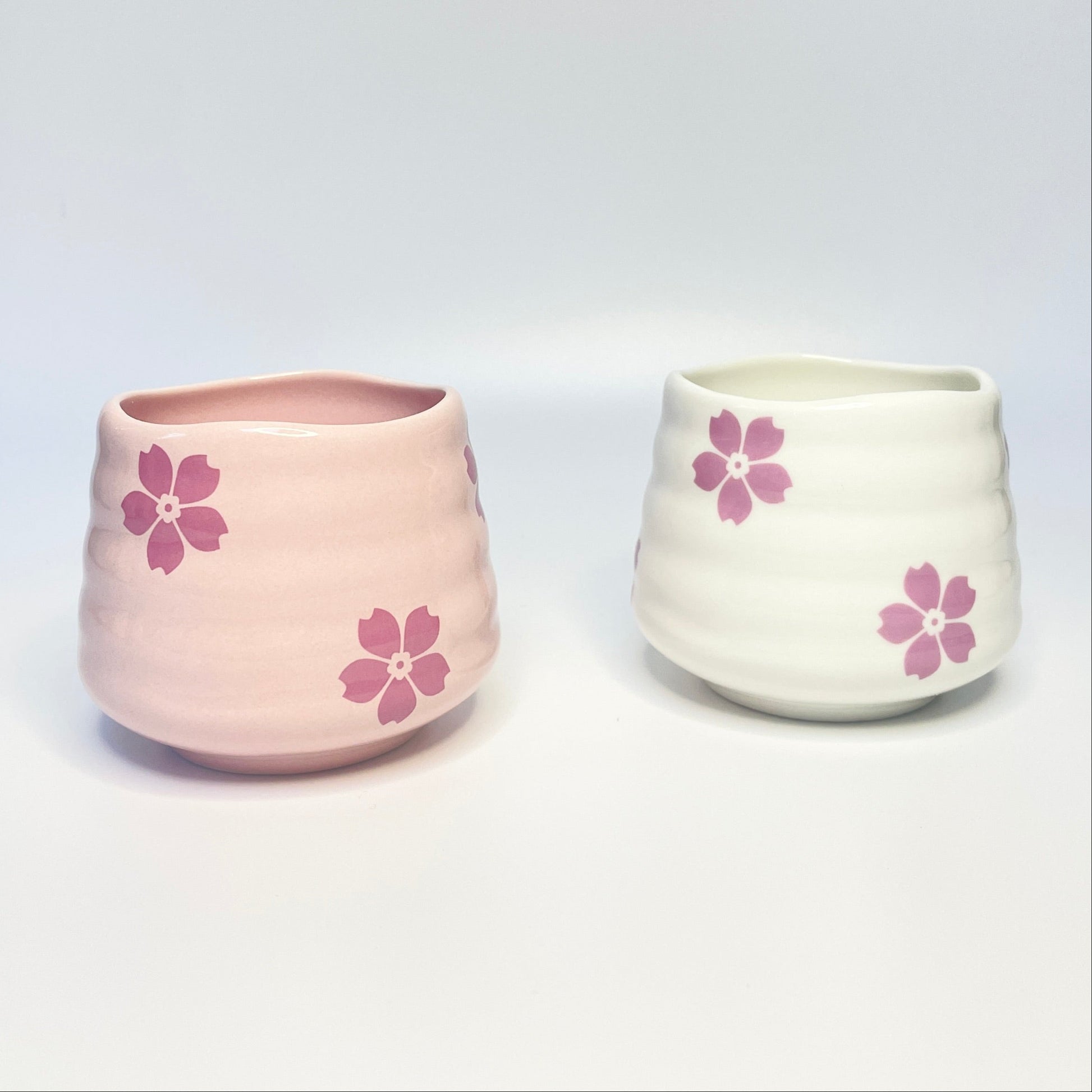 Two ceramic cups/match holders with pink floral designs on a white surface.