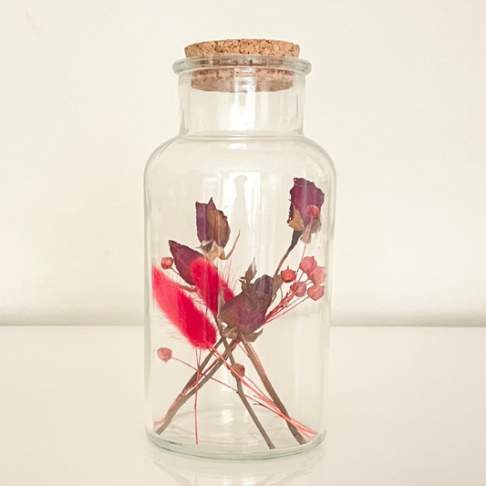 Glass bottle with cork lid containing dried floral arrangements on a white background.