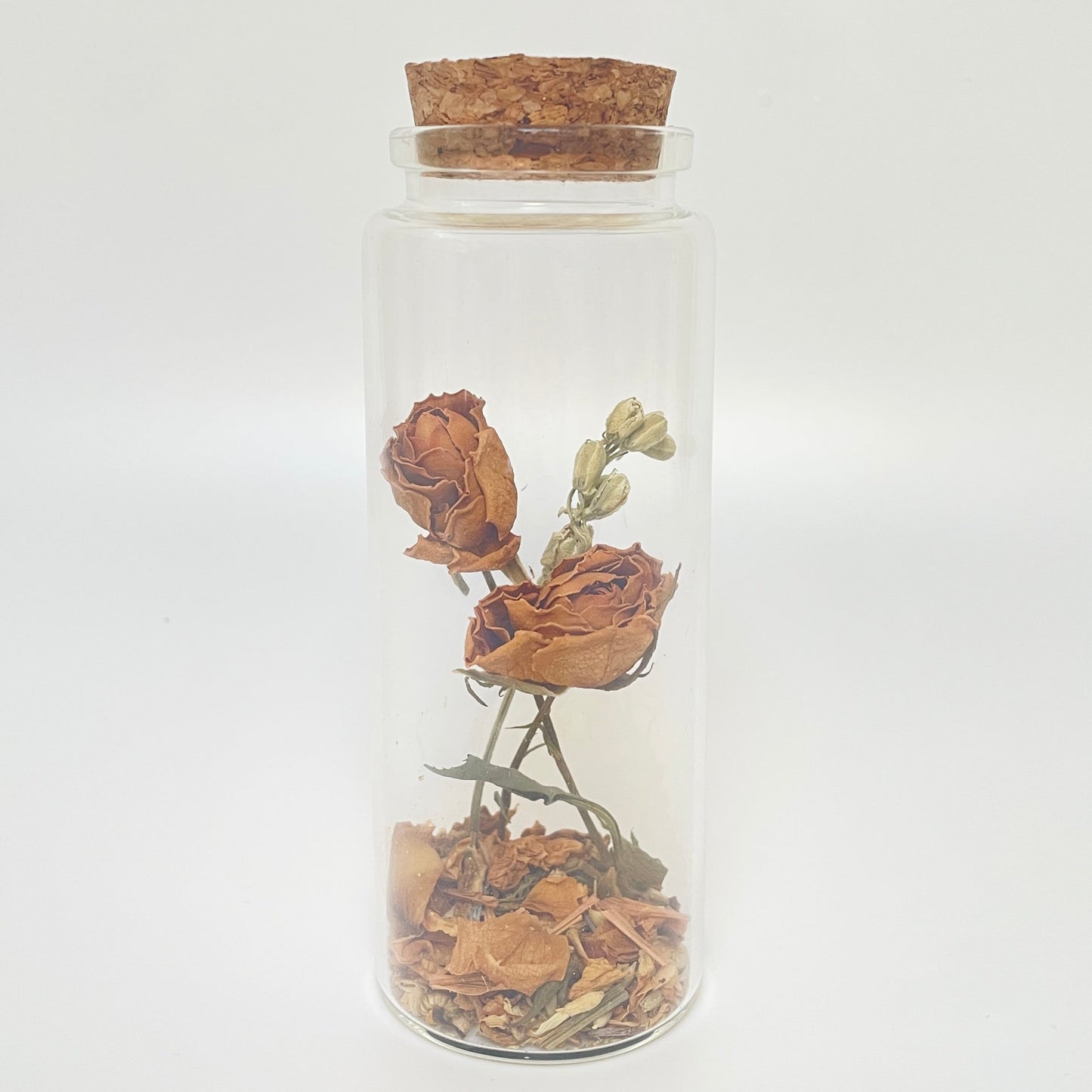Test tube glass bottle filled with dried orange roses and delphinium. 