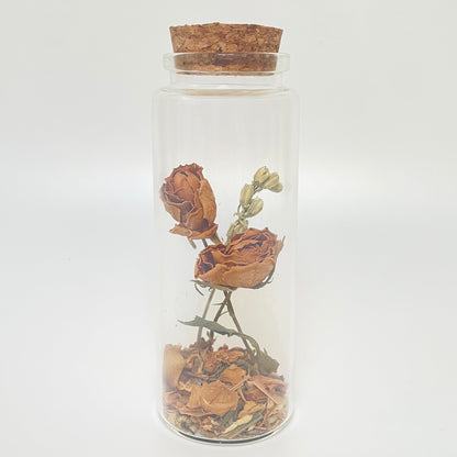 Test tube glass bottle filled with dried orange roses and delphinium. 