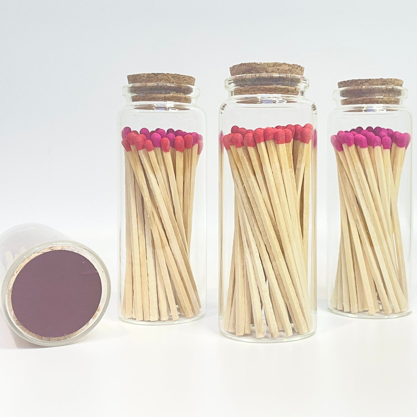 Three glass jars with cork lids containing matches on a white background.