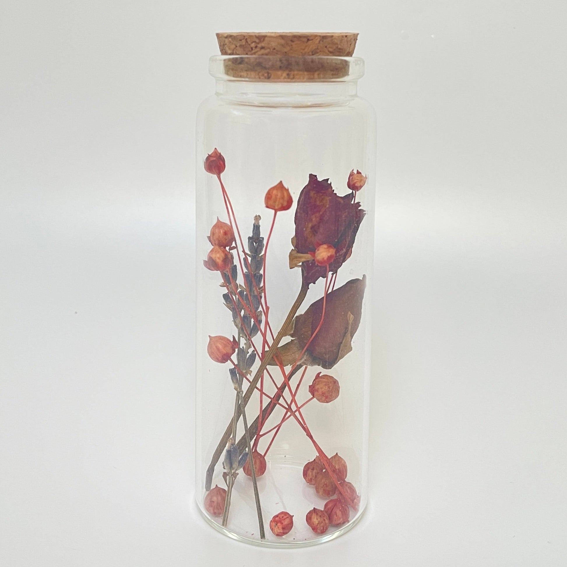 Test tube glass bottle filled with dried red roses and linum flax. 