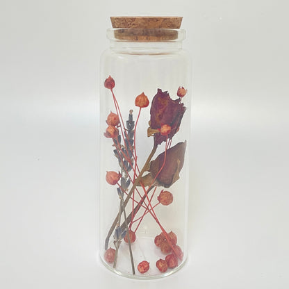 Test tube glass bottle filled with dried red roses and linum flax. 