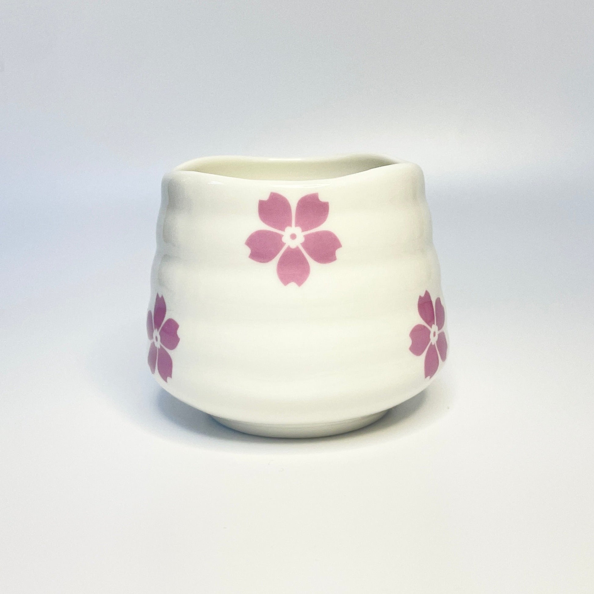 White ceramic match holder/cup with pink floral designs on a white surface.