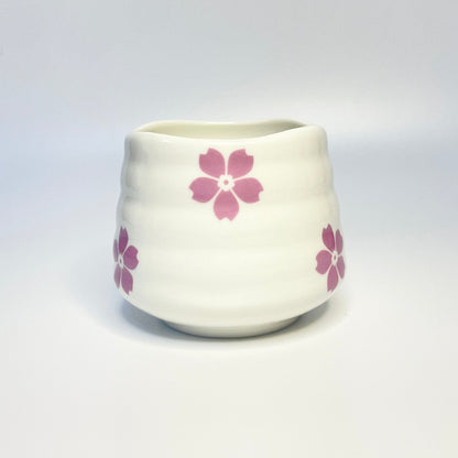 White ceramic match holder/cup with pink floral designs on a white surface.