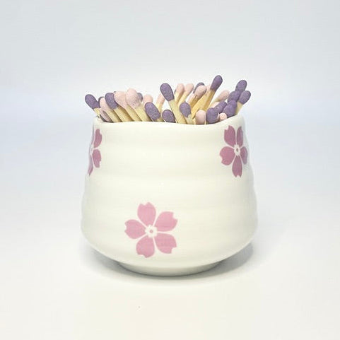 White ceramic holder with flower designs filled with light pink and purple matches on a white background.