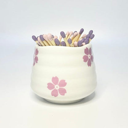 White ceramic holder with flower designs filled with light pink and purple matches on a white background.