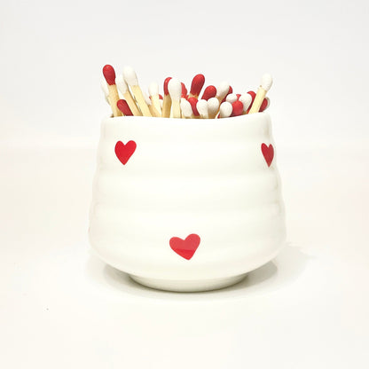 White ceramic holder with heart designs filled with red and white matches on a white background.