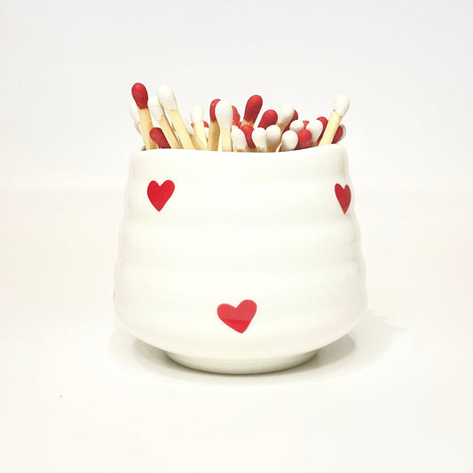 White ceramic holder with heart designs filled with red and white matches on a white background.