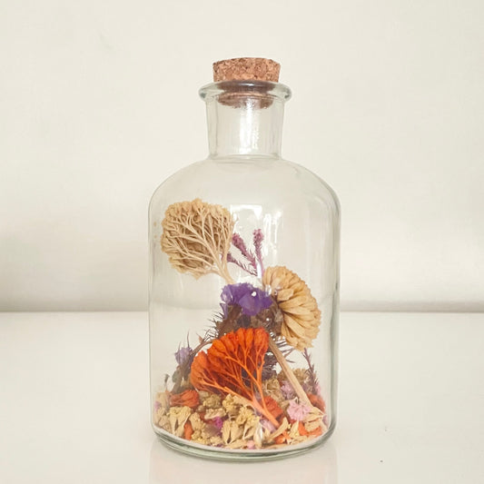 Glass bottle filled with yellow, orange and purple dried flowers on a white background. 