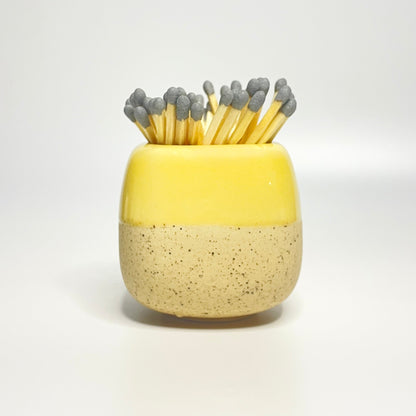Yellow ceramic match holder on a white surface.