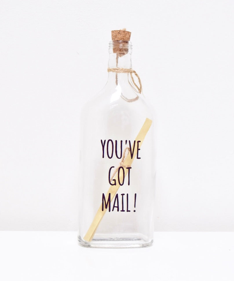 A glass bottle with a message "YOU'VE GOT MAIL" and a cork lid, containing a scroll to write your personalised text.